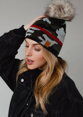Green camo knit pom hat with bold red stripe detail, a natural-toned faux fur pom and cozy fleece lining. A playful winter accessory for chilly days.