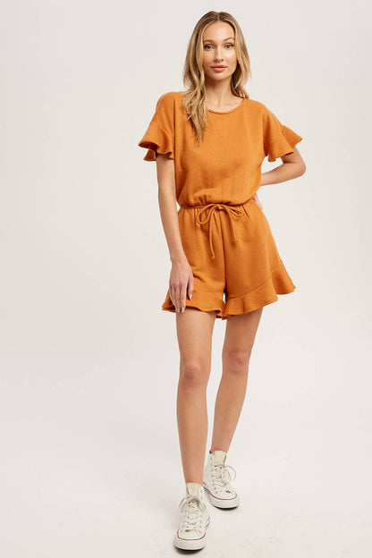 Soft French terry romper with ruffled sleeves, elastic waist, pockets &amp; back button closure. Comfy, cute, and perfect for sunny days or casual outings.