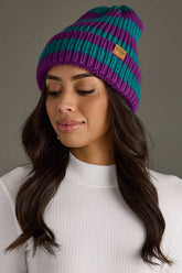 Teal and purple striped chunky knit beanie with a folded cuff and cozy fleece lining. Made from 100% acrylic for warmth and a colorful winter look.