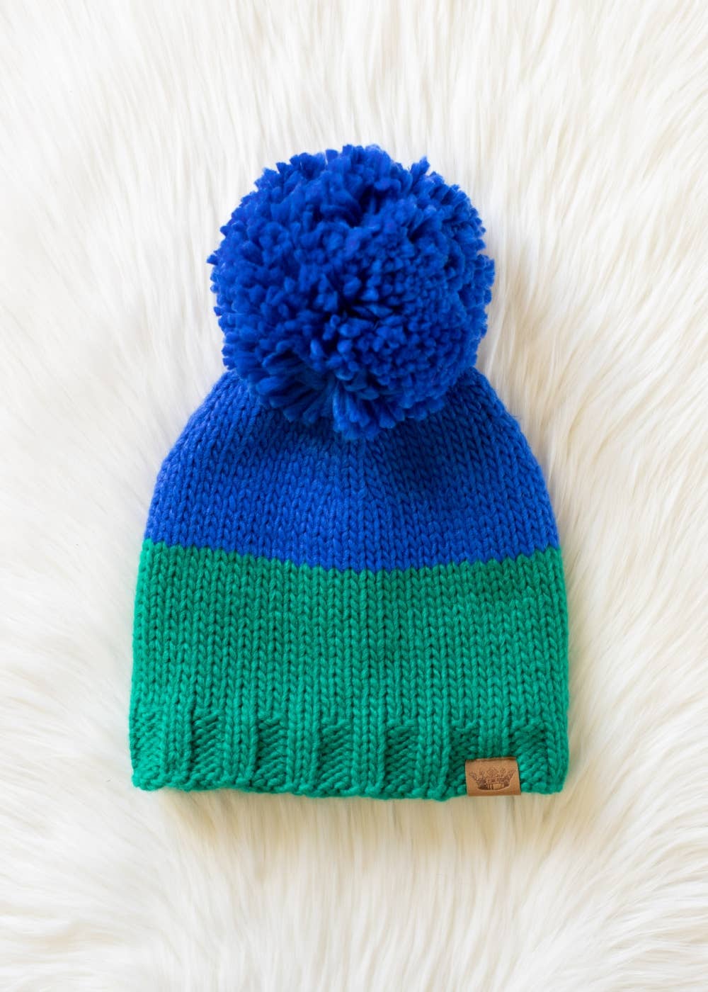 Blue and green color block pom hat by Panache Apparel Co. Made from 100% acrylic with cozy fleece lining and a large pom for cheerful winter style.