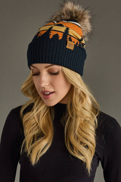 Dark navy knit hat with forest landscape design &amp; natural faux fur pom. Warm, stretchy, and stylish—crafted from 85% acrylic &amp; 15% spandex for comfort.