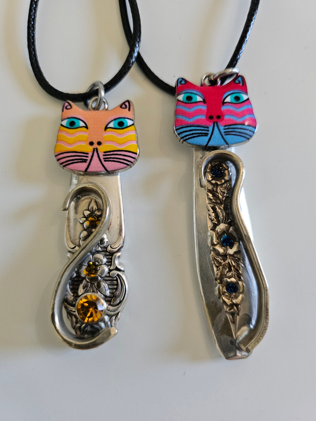 Handcrafted vintage silverware necklaces featuring enamel cat faces on adjustable satin cords. Made from 1951 Distinction and 1952 Primrose patterns.