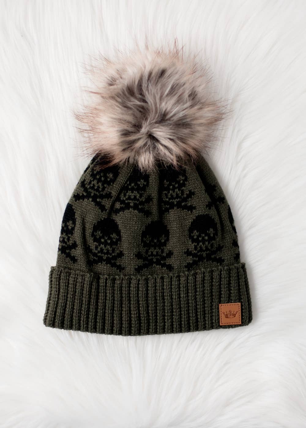 Olive skull pattern knit hat with natural faux fur pom. Fleece lined for cozy warmth and style. 100% acrylic and pairs perfectly with matching mittens.