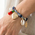 Heart Locket & Charms Bandana Bracelet featuring a heart locket, cowrie shell, feather, and seaside-inspired charms on a vintage-style fabric band.