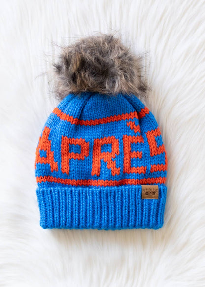 Blue and orange Après knit hat with a natural-toned faux fur pom and cozy fleece lining. Made from 100% acrylic for colorful, comfortable winter style.
