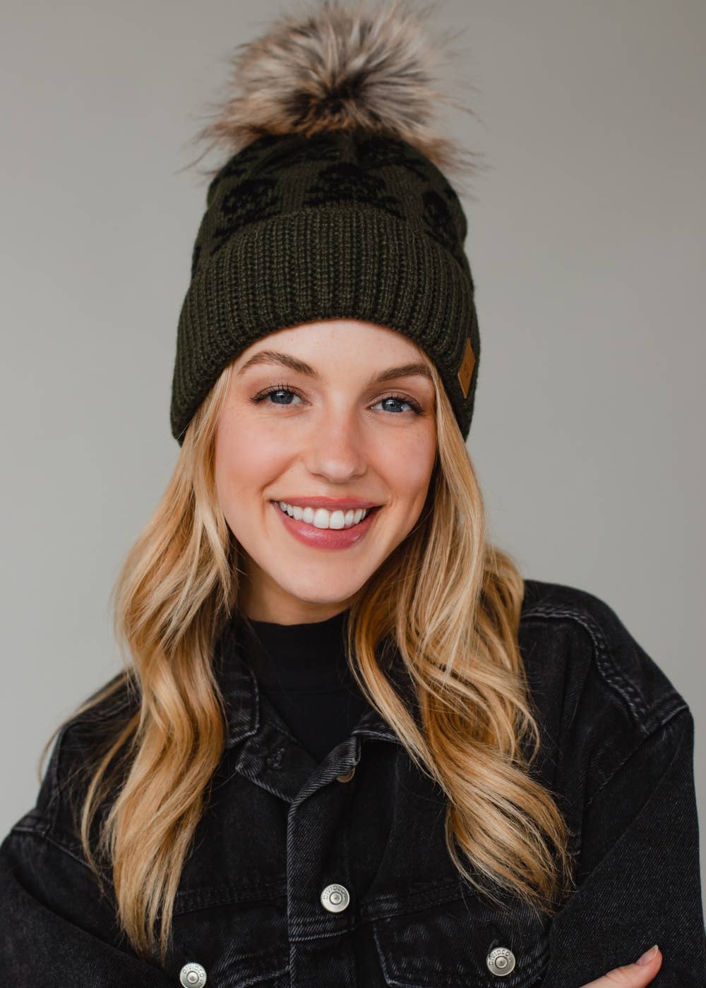 Olive skull pattern knit hat with natural faux fur pom. Fleece lined for cozy warmth and style. 100% acrylic and pairs perfectly with matching mittens.