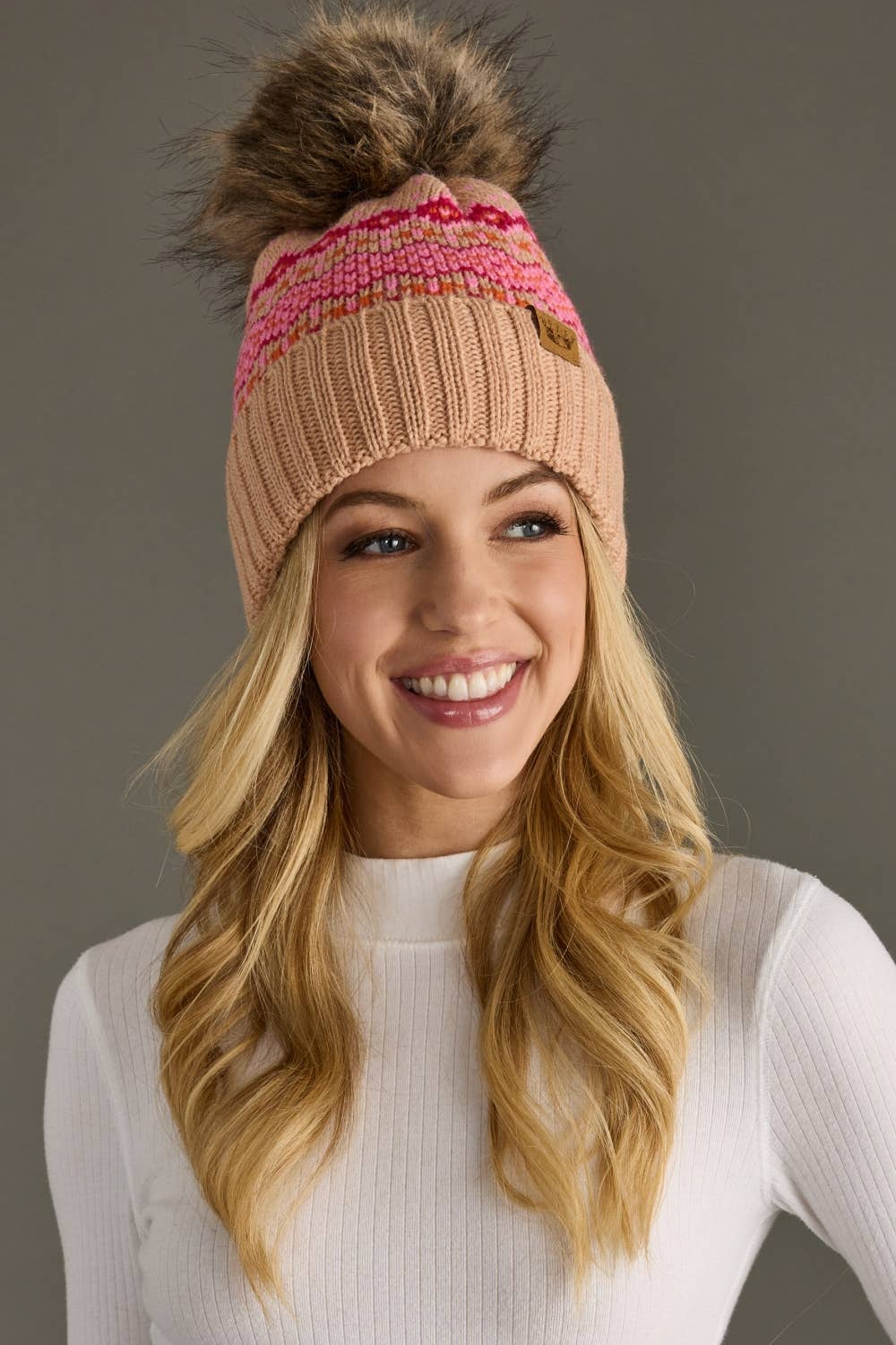 Blush, pink & orange patterned knit hat with natural faux fur pom. Fleece lined for extra warmth & pairs perfectly with matching mittens. 100% acrylic.