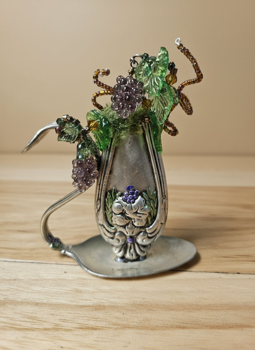 Vintage silverware bud vase with handcrafted beaded flowers by artist KStonely. Unique, eco-friendly cottagecore décor perfect for shelves, desks, and gifting.