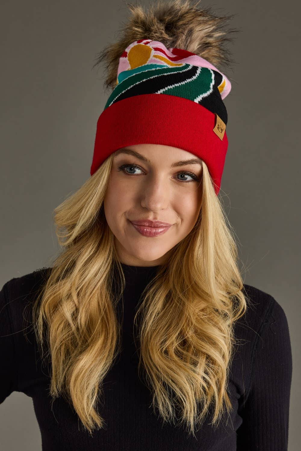 Red & pink sunrise landscape knit hat with natural faux fur pom. Warm, soft, and stretchy blend of 85% acrylic & 15% spandex—cozy winter style with flair.