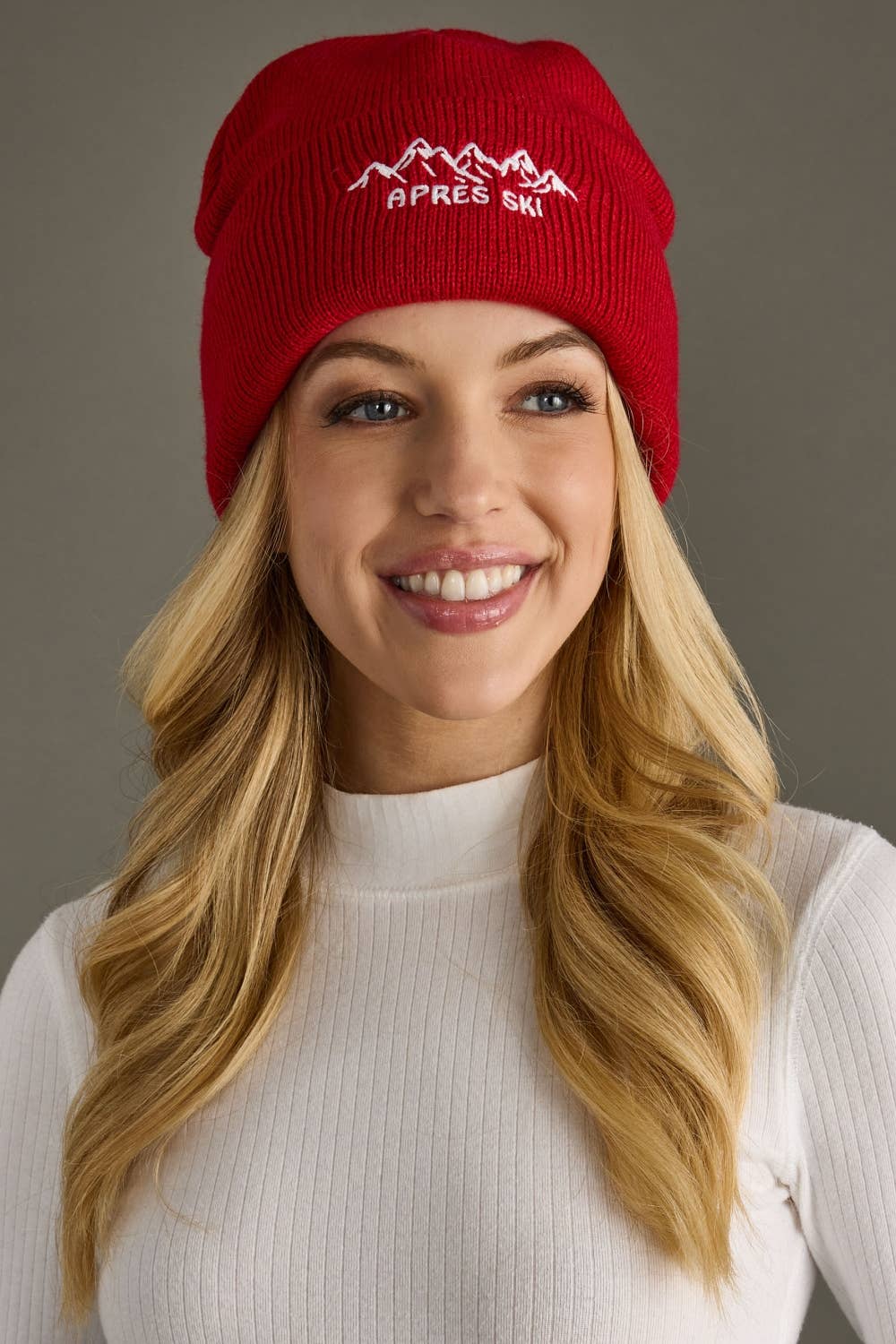 Red knit beanie with white embroidered Apres Ski text and graphic on the cuff. Fleece lined and made from 100% acrylic for cozy, playful winter style.
