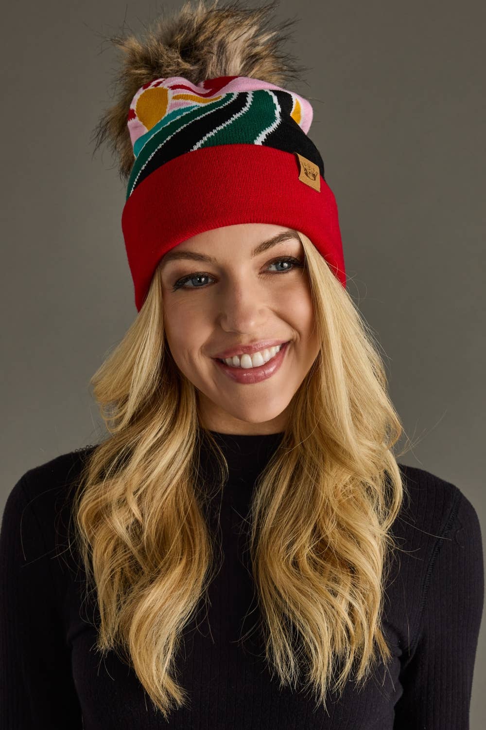 Red & pink sunrise landscape knit hat with natural faux fur pom. Warm, soft, and stretchy blend of 85% acrylic & 15% spandex—cozy winter style with flair.