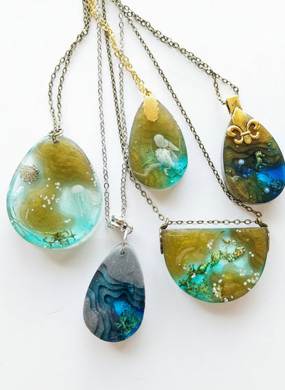 Sea Life Resin Pendant Necklaces by artist KStonely featuring shells, fish, jellyfish, and sea life miniatures in dreamy blue, brown, and gold ocean-inspired resin.