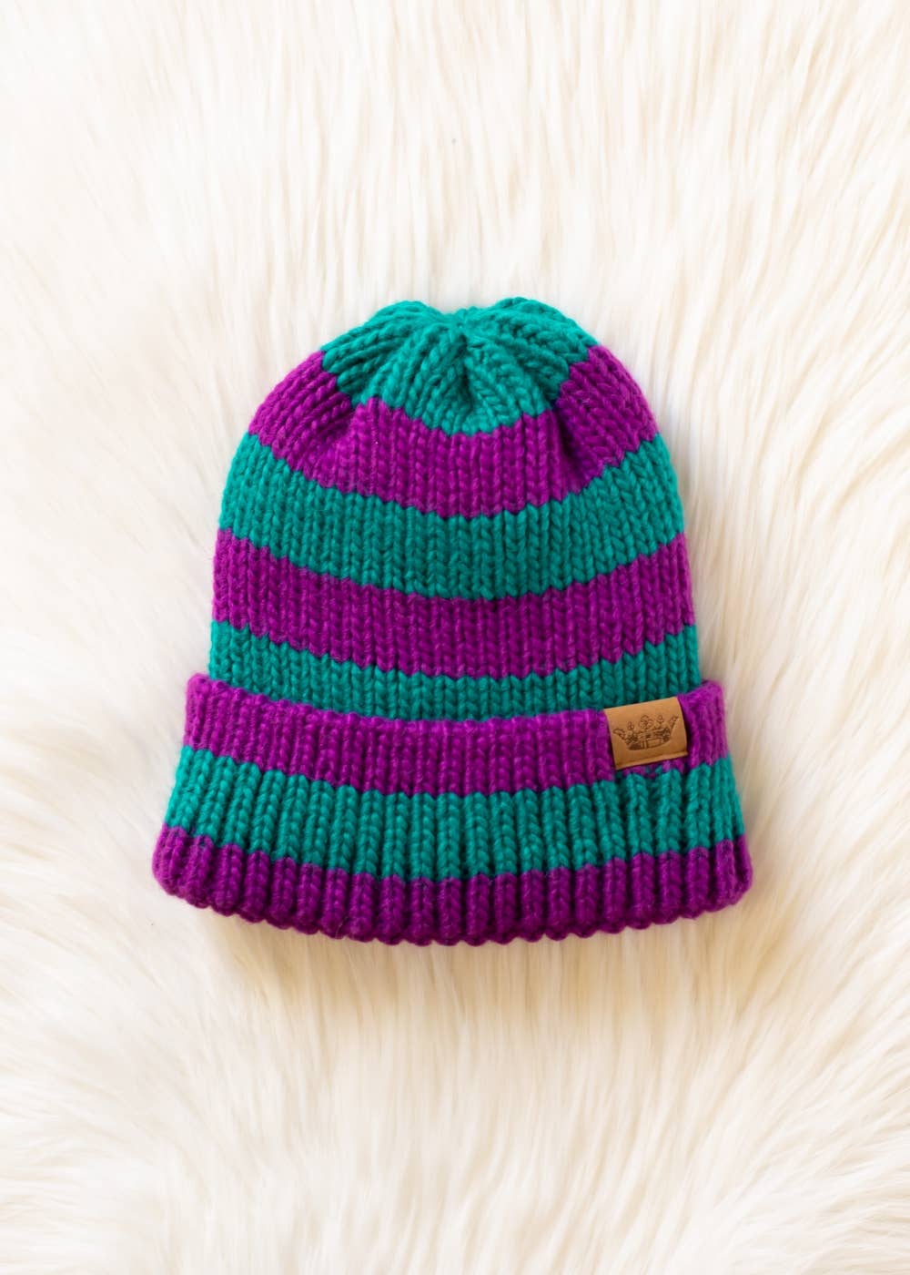 Teal and purple striped chunky knit beanie with a folded cuff and cozy fleece lining. Made from 100% acrylic for warmth and a colorful winter look.